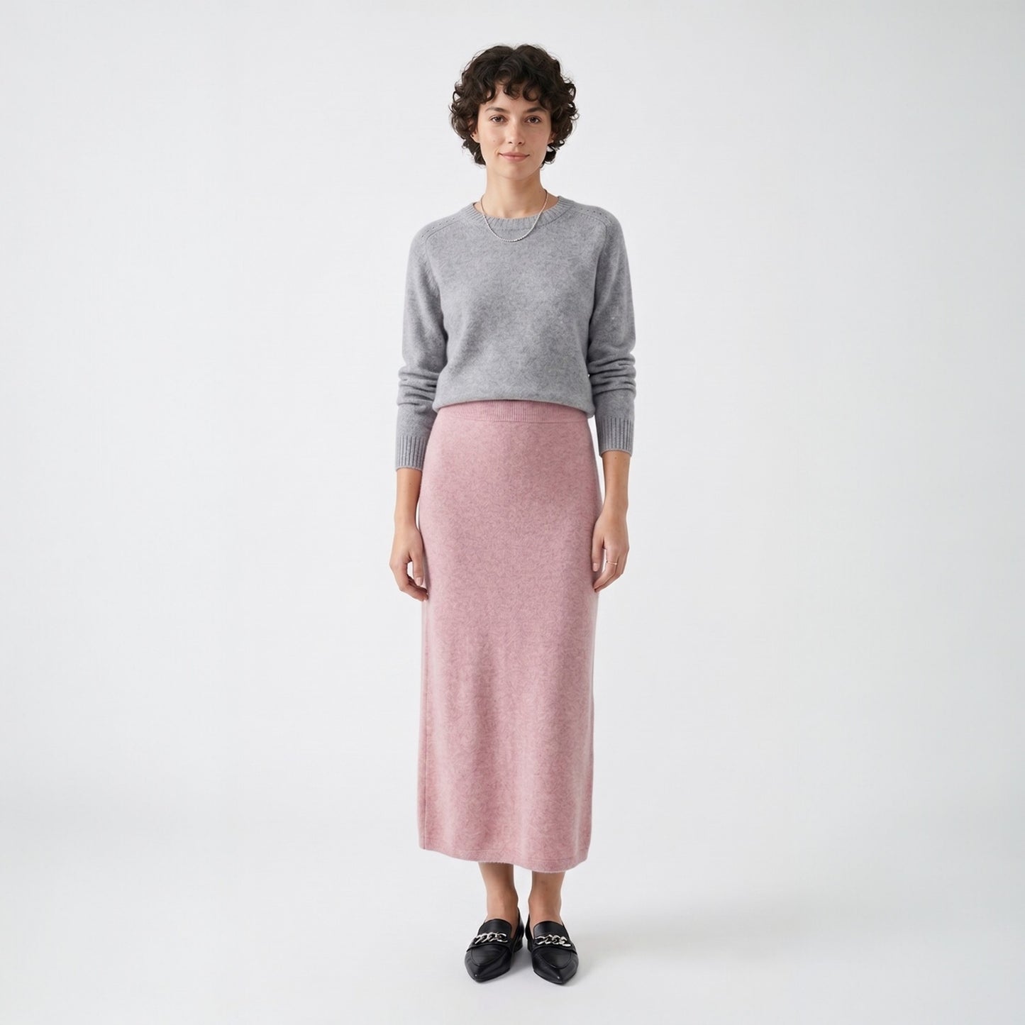 Model styling the rose pink knit midi skirt with a grey crew neck sweater and black loafers for a smart casual look.