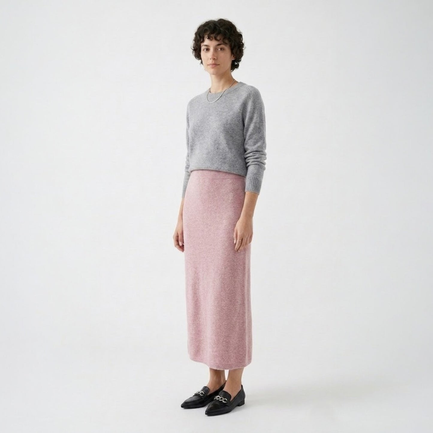 Model styling the rose pink knit midi skirt with a grey crew neck sweater and black loafers for a smart casual look.