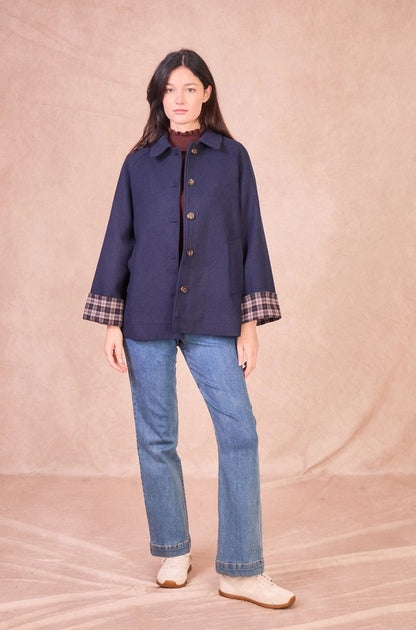 Front full-length view of a model wearing a navy wool-blend jacket with a tailored collar, button closure, and plaid turned-up cuffs styled with jeans.