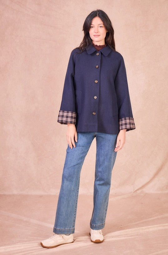Front full-length view of a model wearing a navy wool-blend jacket with a tailored collar, button closure, and plaid turned-up cuffs styled with jeans.